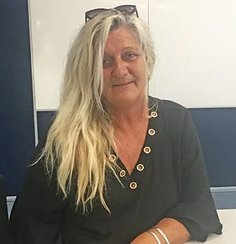 A woman with long fair hair sitting at a desk, smiling at the camera.