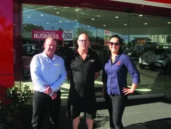 Three people standing together outside the glass front of a Toyota dealership.