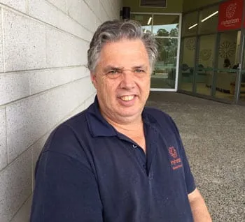 A man in a navy Myhorizon polo shirt standing outside the Capalaba centre entrance, smiling at the camera.