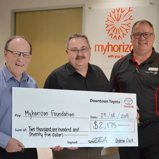 Three men holding an oversized cheque from Downtown Toyota to the Myhorizon Foundation for two thousand, one hundred and seventy five dollars, in front of the Myhorizon logo on the wall.