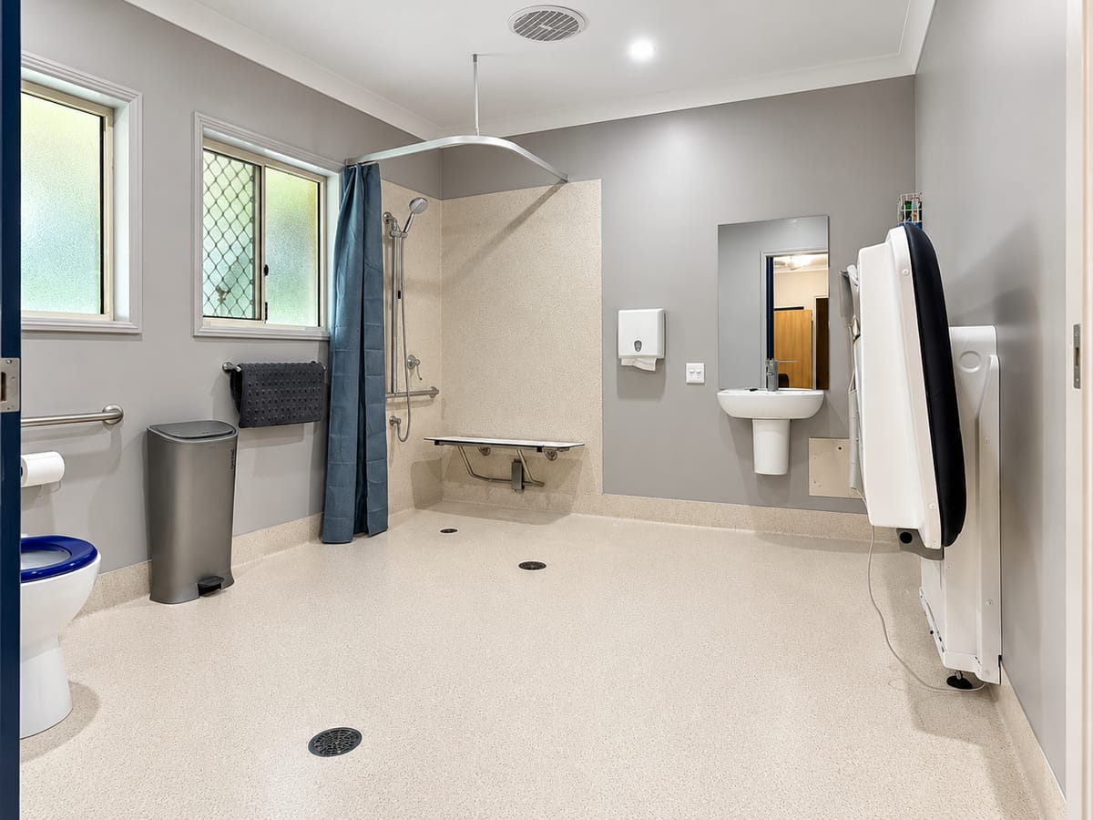 The accessible bathroom at our Alexandra Hills short stay house, with a step-free shower, a fold-down shower seat, grab rails and a fold-up change table.