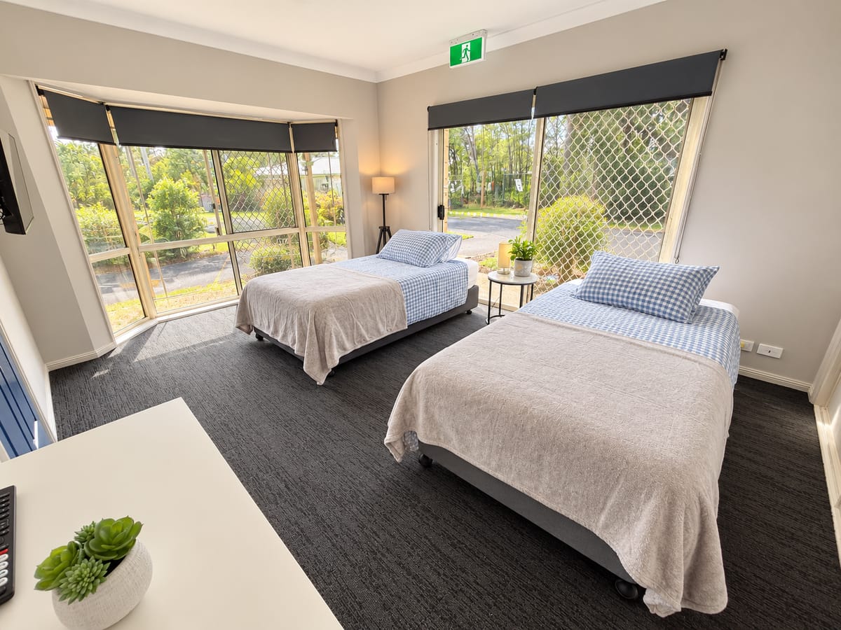 A twin room with a bay window at our Alexandra Hills short stay house, with two beds made in blue gingham and grey throws.